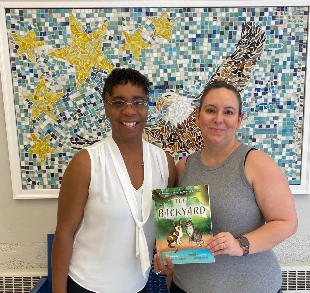 Two women standing in front of a wall with a book.