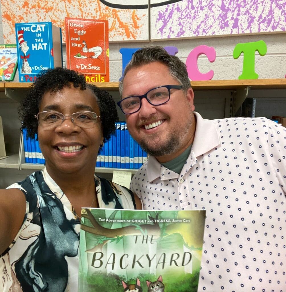 A man and woman pose with a book in front of a library.