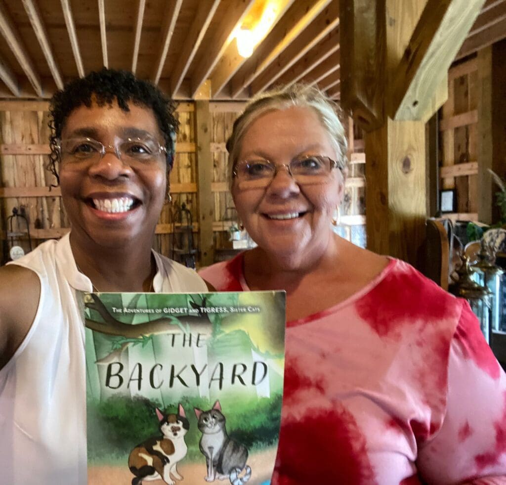 Two women standing next to each other holding a book.