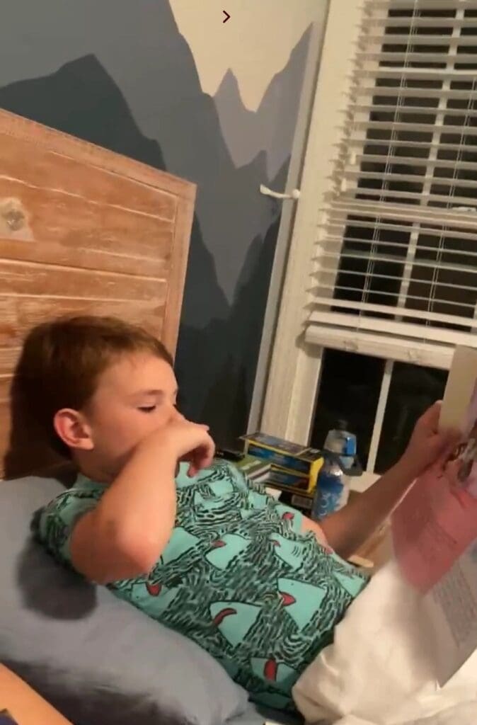 A boy laying in bed reading a book.