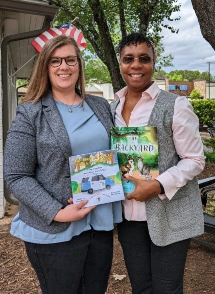 Two women standing next to each other holding books.