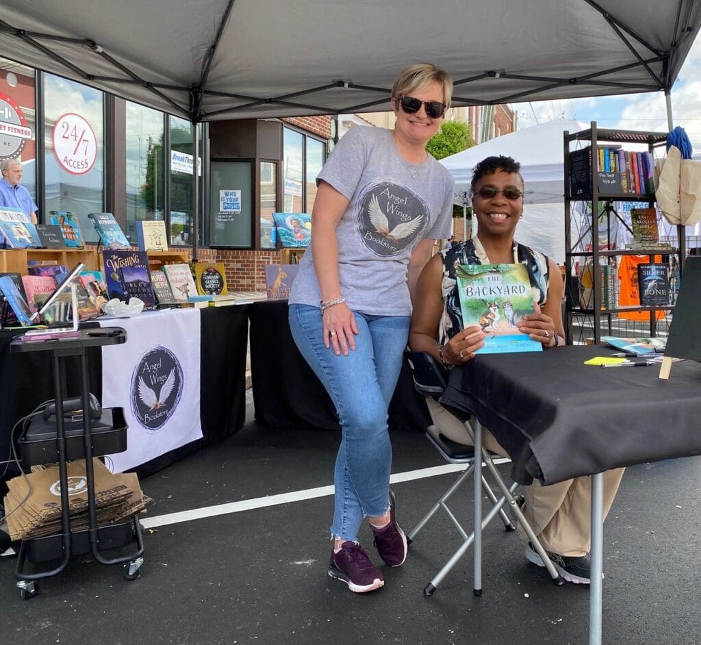 Two women sitting at a table with a book in front of them.