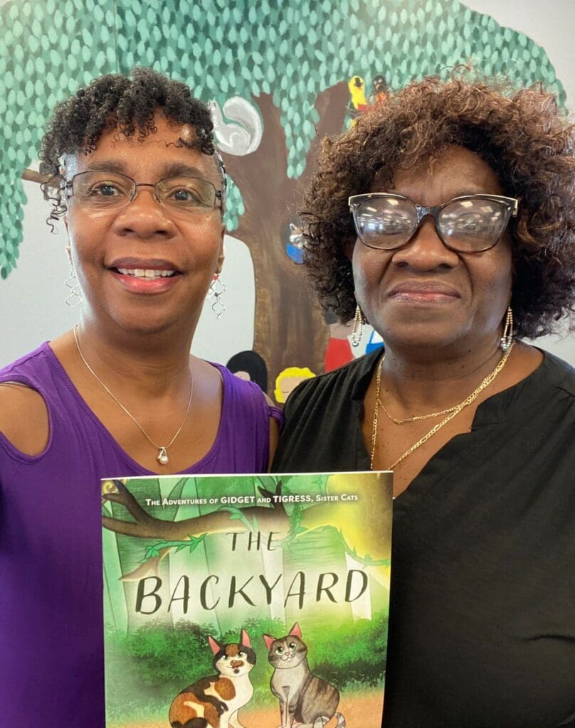 Two women standing next to each other holding a book.