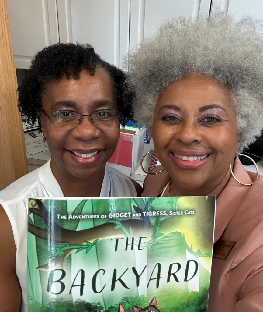 Two women standing next to each other holding a book.