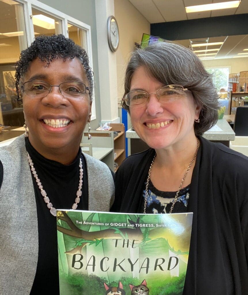 Two women standing next to each other holding a book.