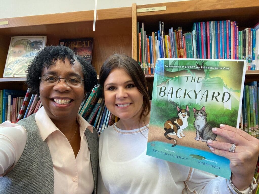 Two women standing in front of a bookshelf holding a book.