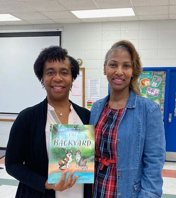 Two women standing next to each other holding a book.