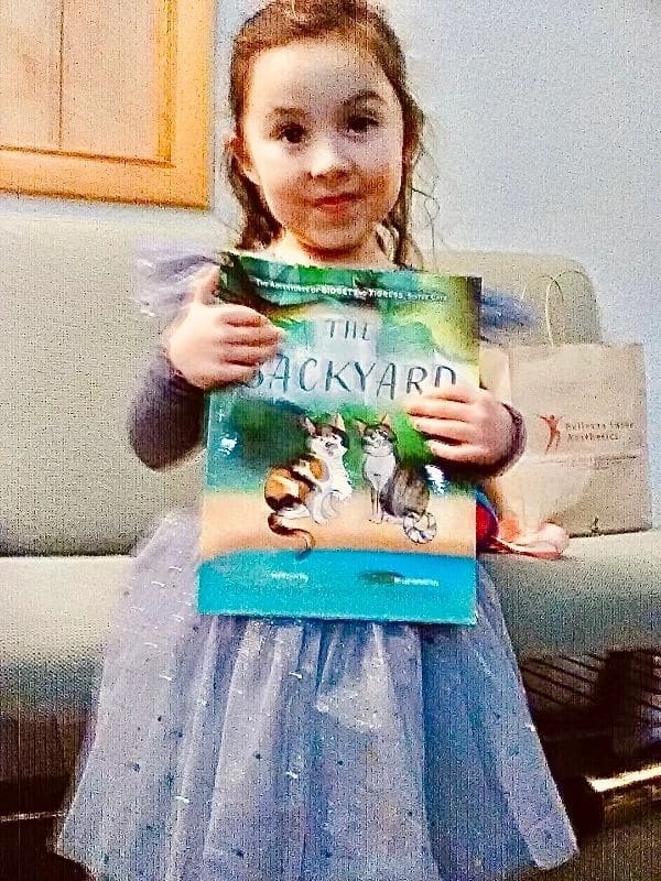 A little girl holding up a book in front of a couch.