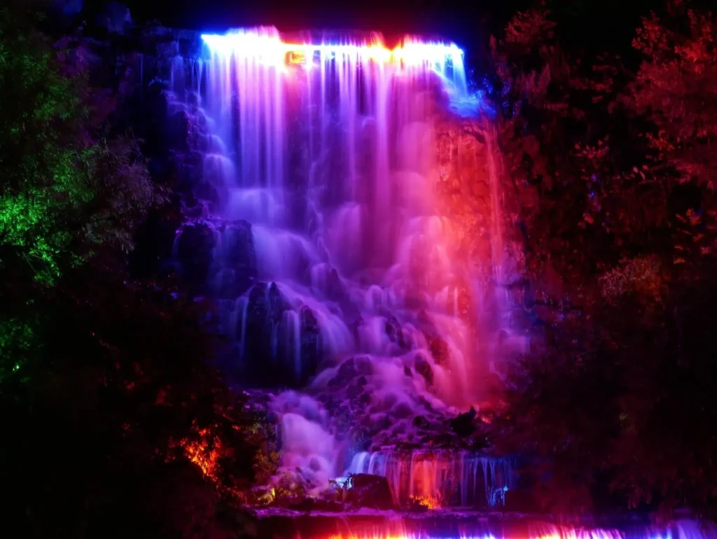 Illuminated waterfall with colorful lights at night.