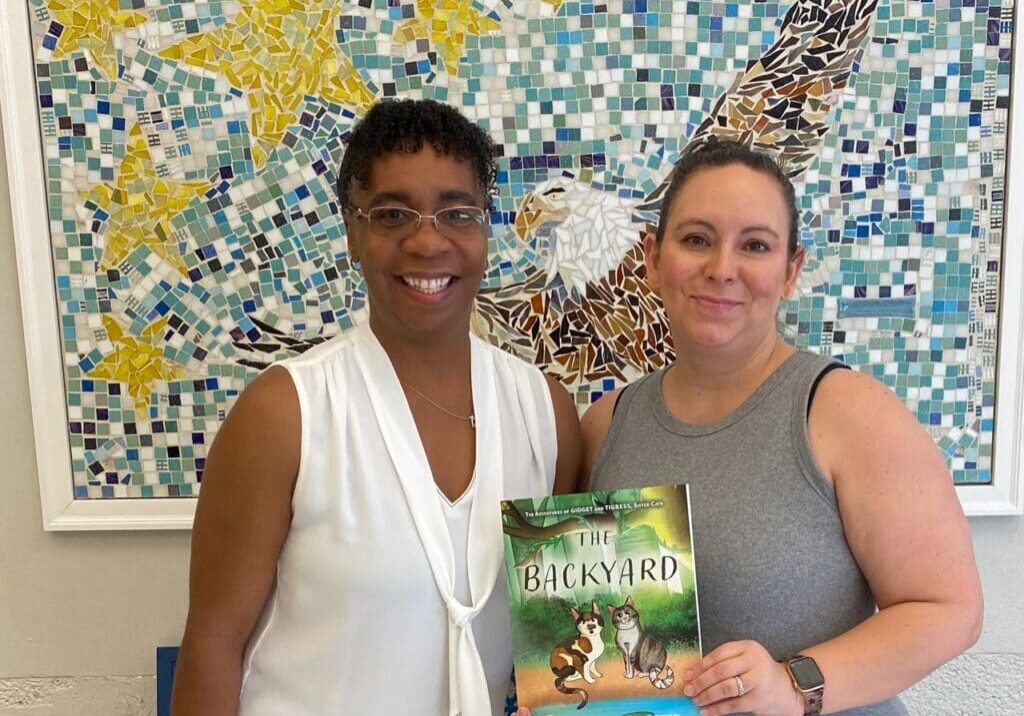 Two women standing in front of a wall with a book.