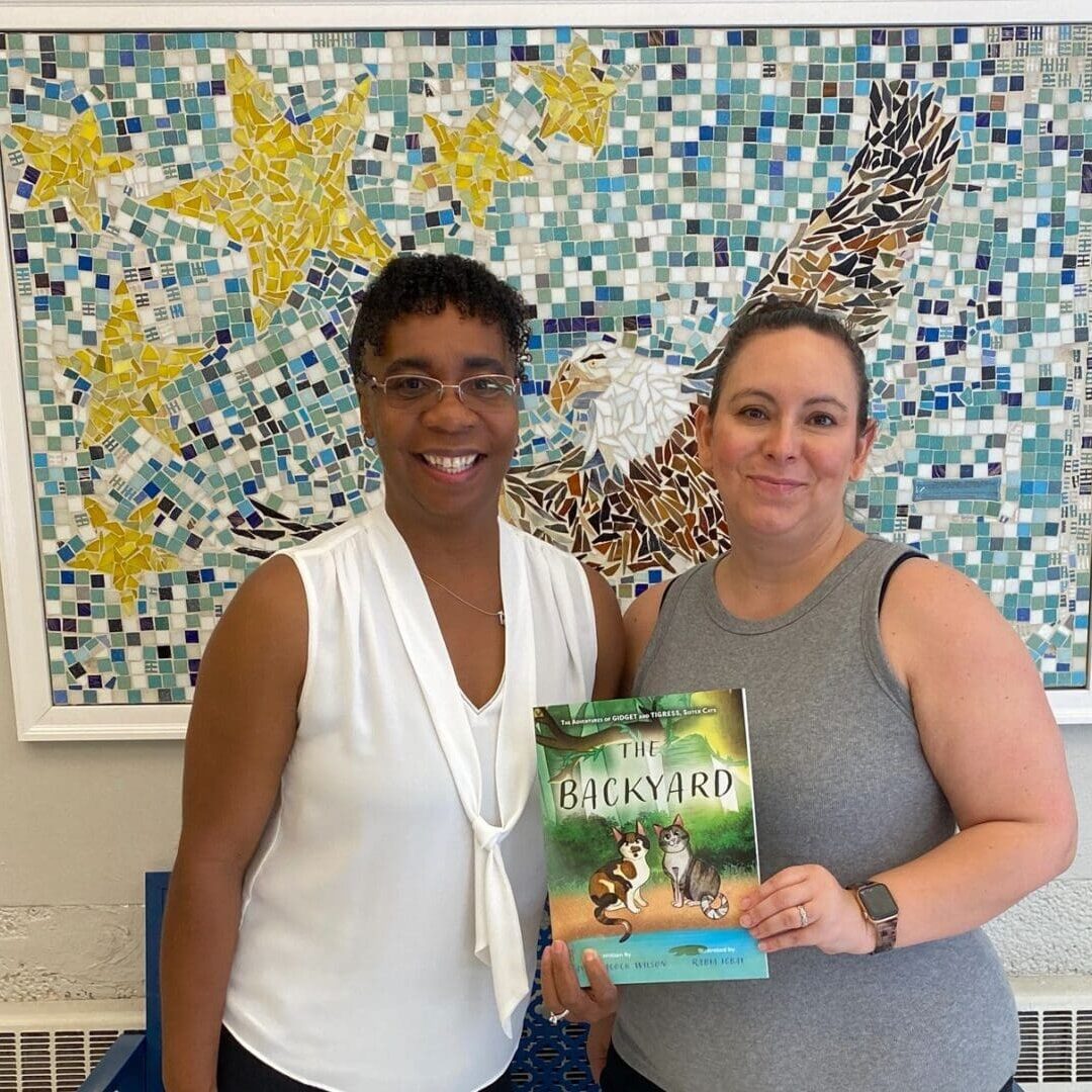 Two women standing in front of a wall with a book.