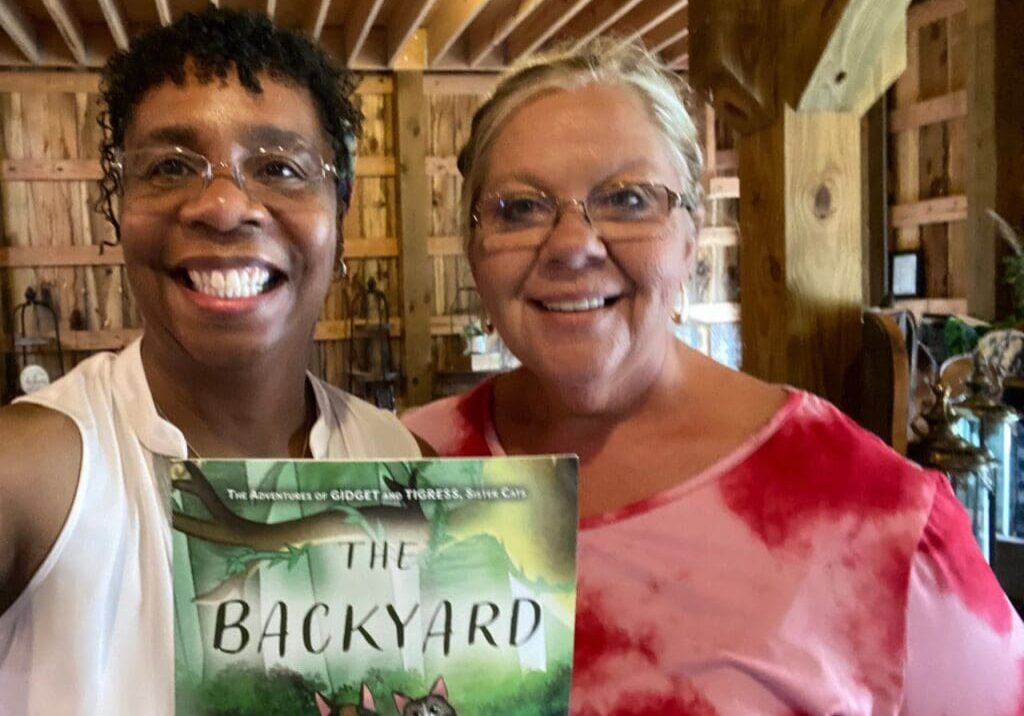 Two women standing next to each other holding a book.