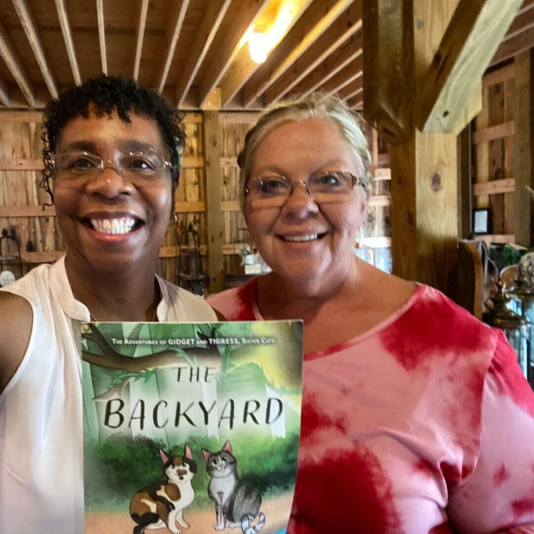 Two women standing next to each other holding a book.