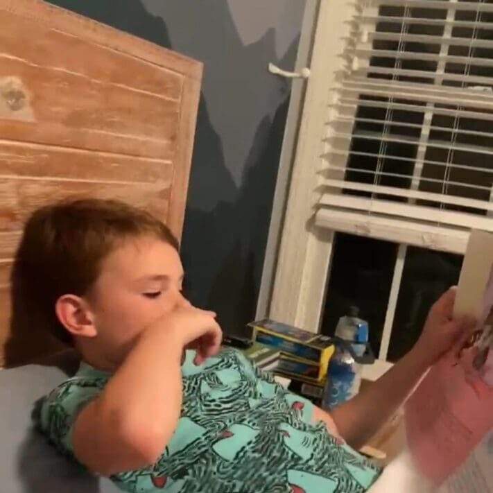 A boy laying in bed reading a book.