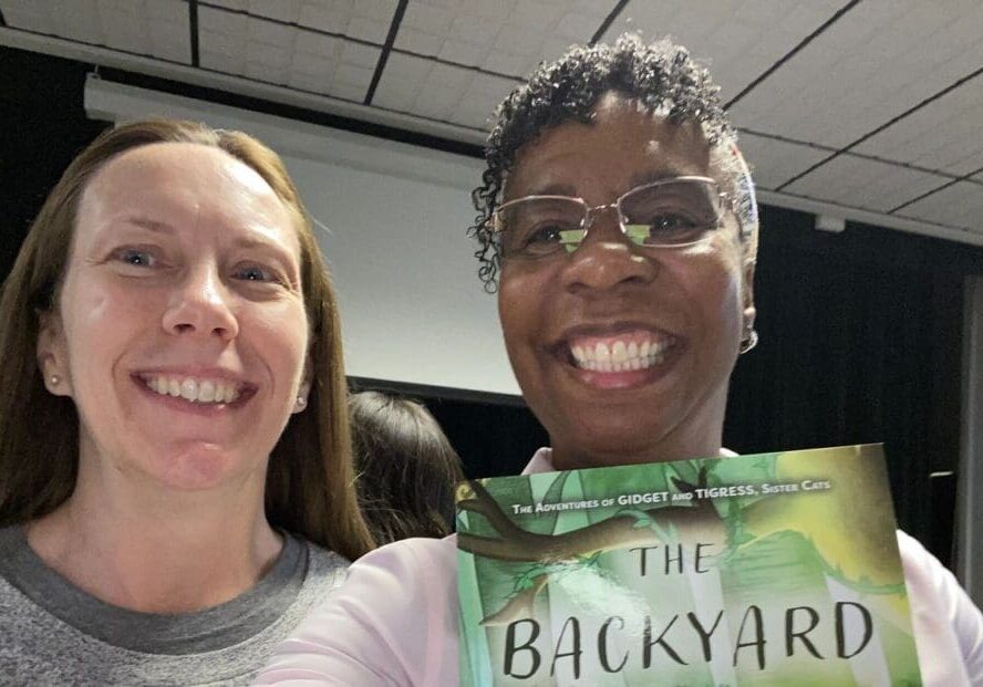 Two women smiling with a book in their hands.