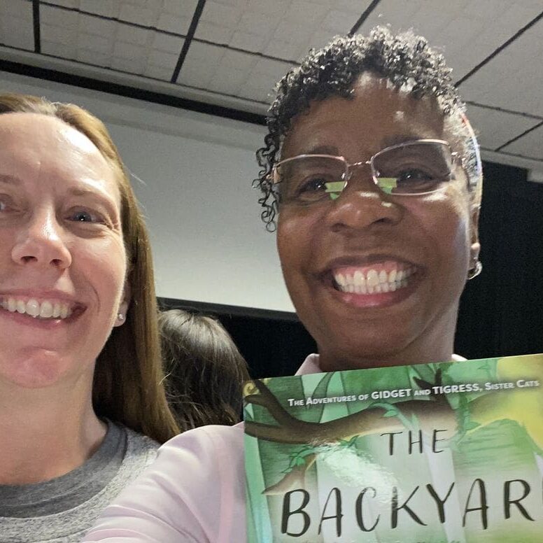 Two women smiling with a book in their hands.