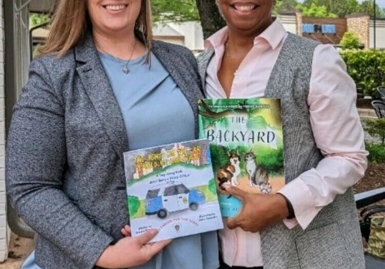 Two women standing next to each other holding books.