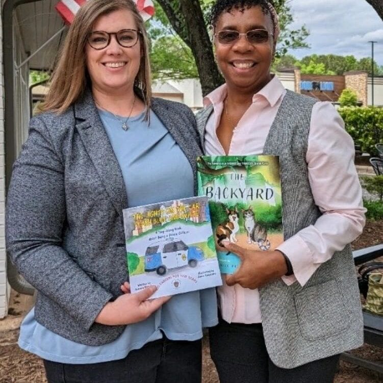 Two women standing next to each other holding books.