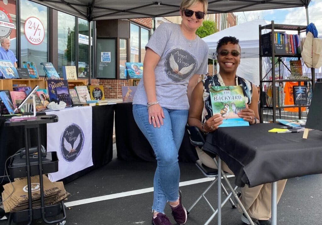 Two women sitting at a table with a book in front of them.