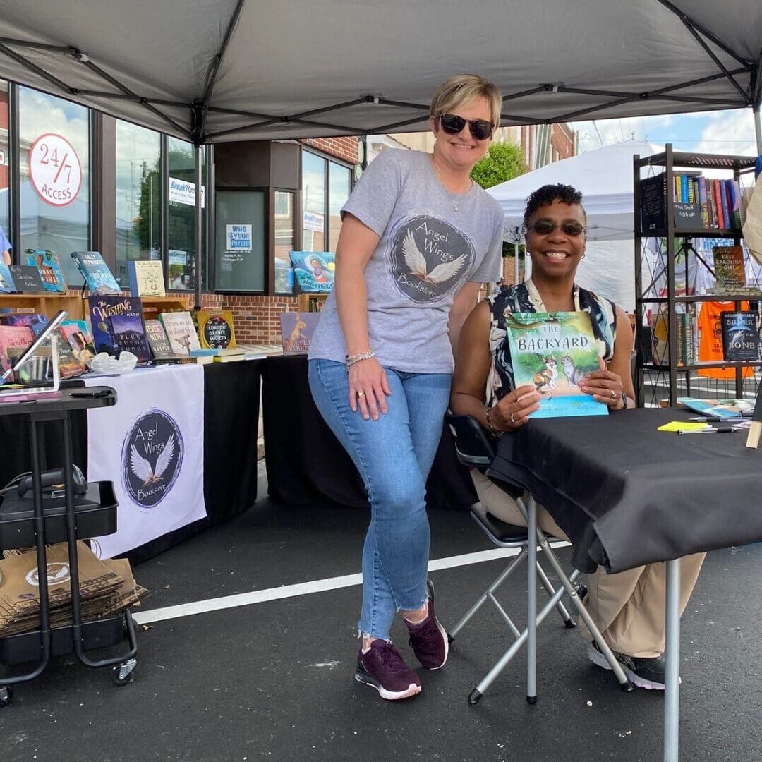 Two women sitting at a table with a book in front of them.