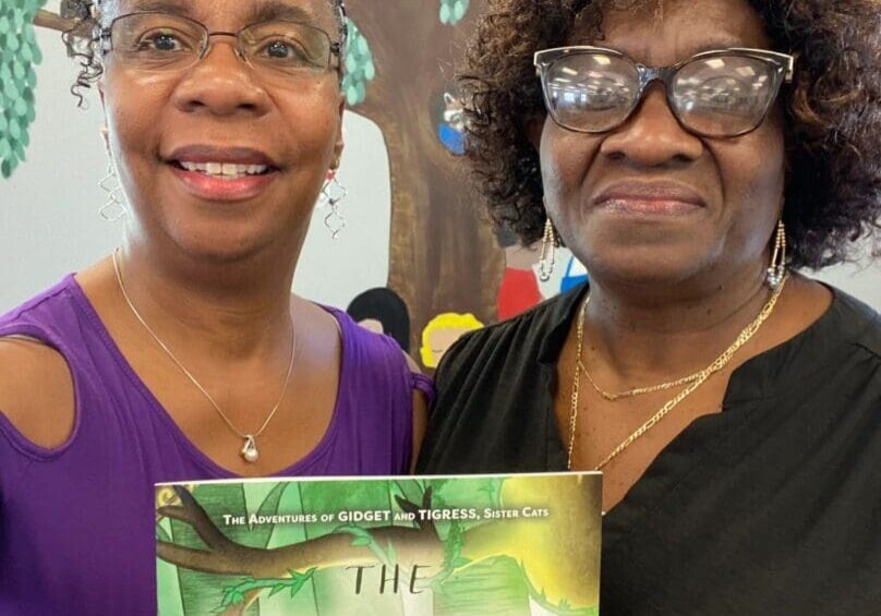 Two women standing next to each other holding a book.