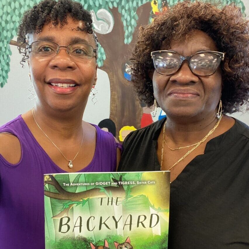 Two women standing next to each other holding a book.