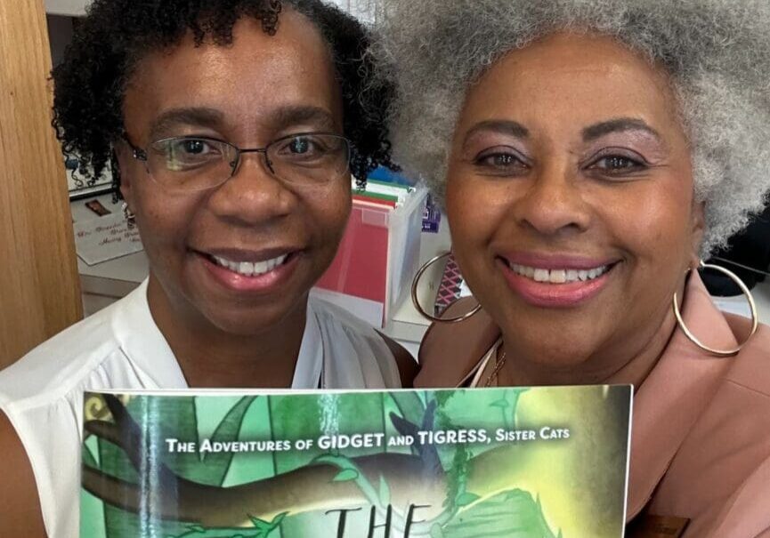 Two women standing next to each other holding a book.