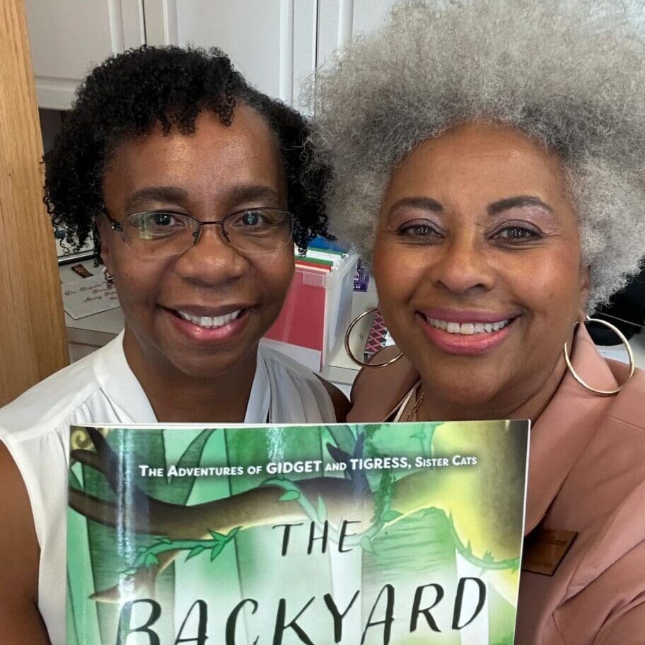 Two women standing next to each other holding a book.