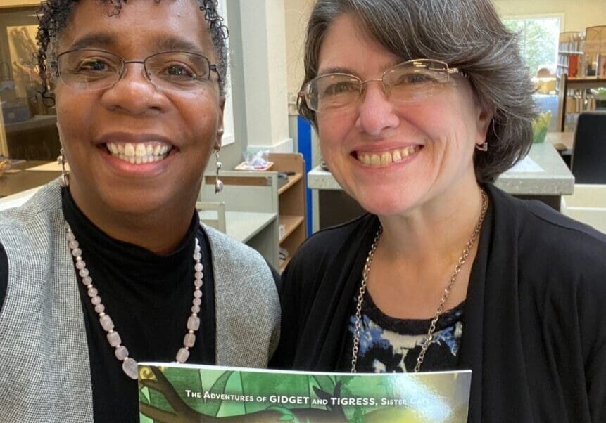 Two women standing next to each other holding a book.