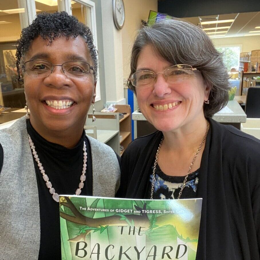 Two women standing next to each other holding a book.