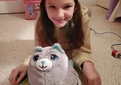 A girl sitting on the floor next to a stuffed animal.