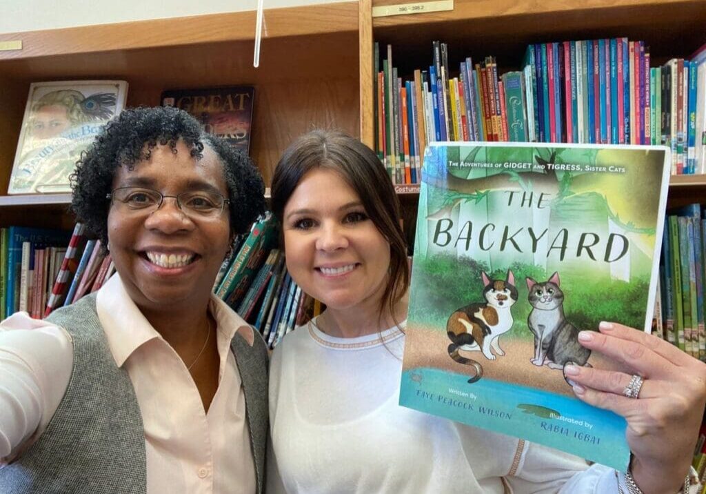 Two women standing in front of a bookshelf holding a book.