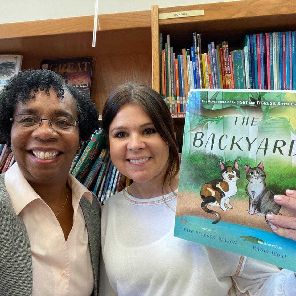 Two women standing in front of a bookshelf holding a book.