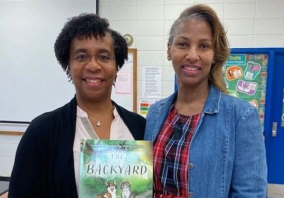 Two women standing next to each other holding a book.