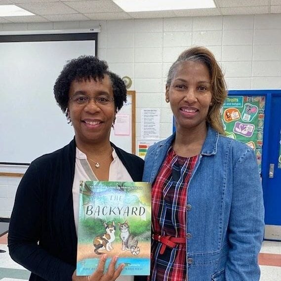 Two women standing next to each other holding a book.