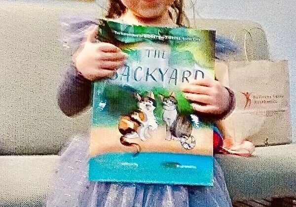 A little girl holding up a book in front of a couch.