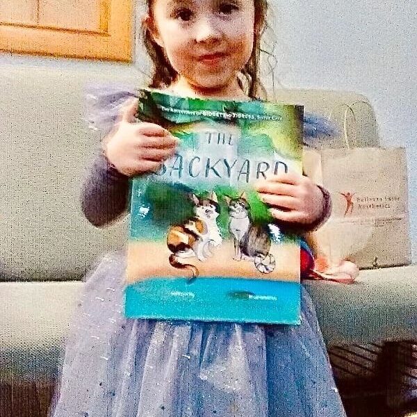 A little girl holding up a book in front of a couch.