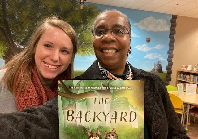 Two women holding up a book in a library.